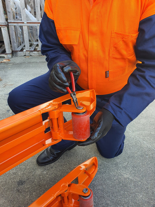 Person in orange and blue work attire using a tool on an orange piece of equipment.