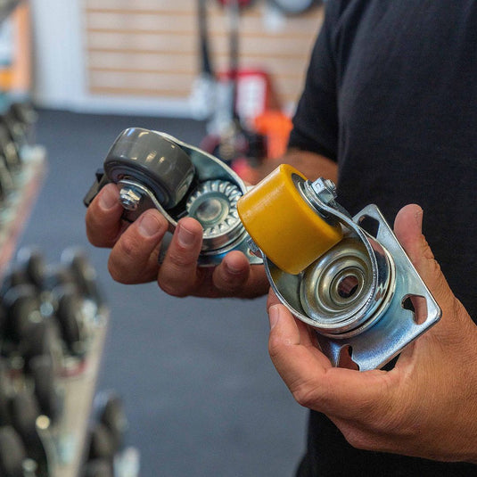 An adult man, employee holding two different castors, one wheel yellow and the other grey